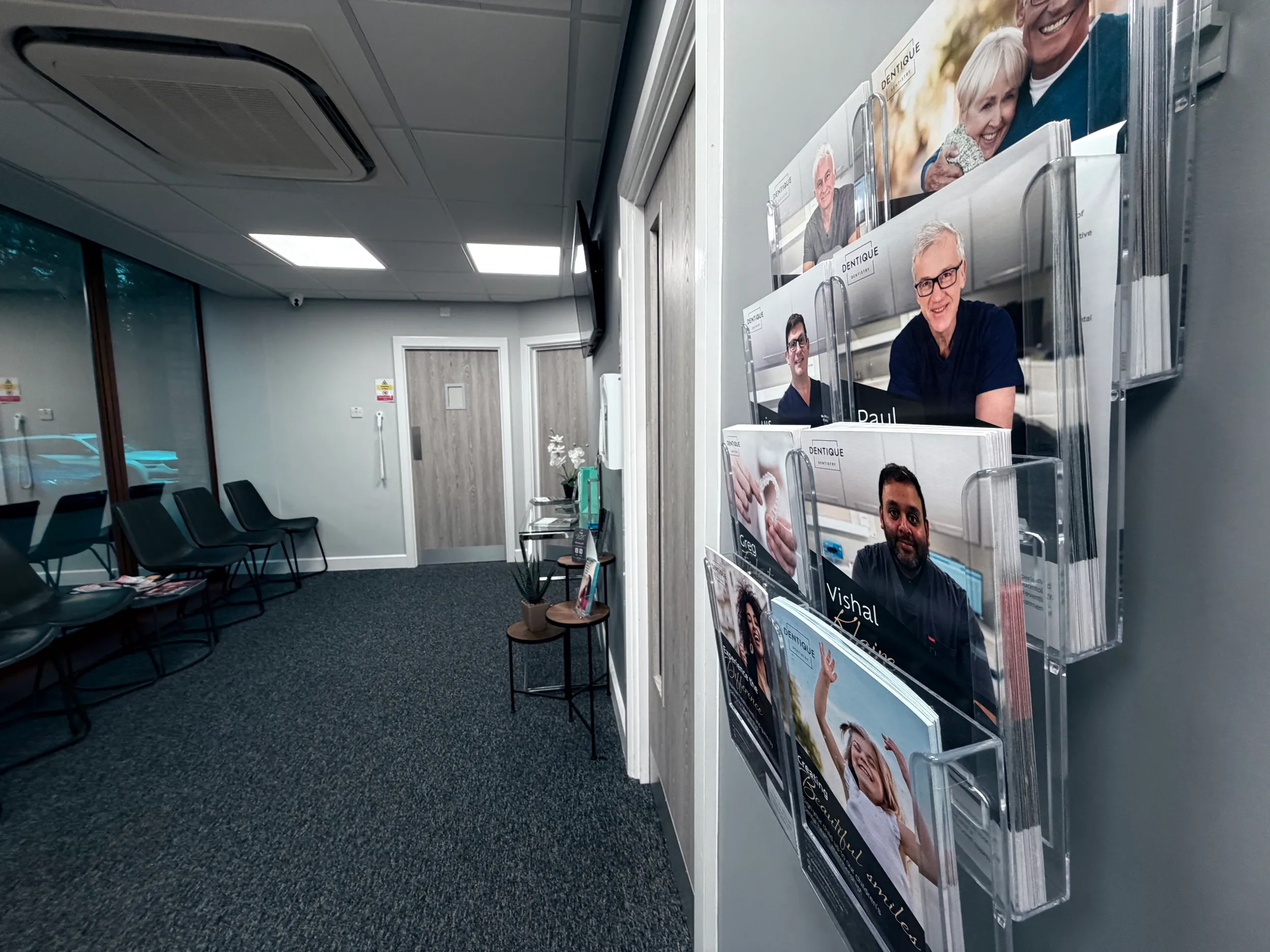 Waiting room with black chairs, a display rack holding dental brochures, and two wooden doors in the background.