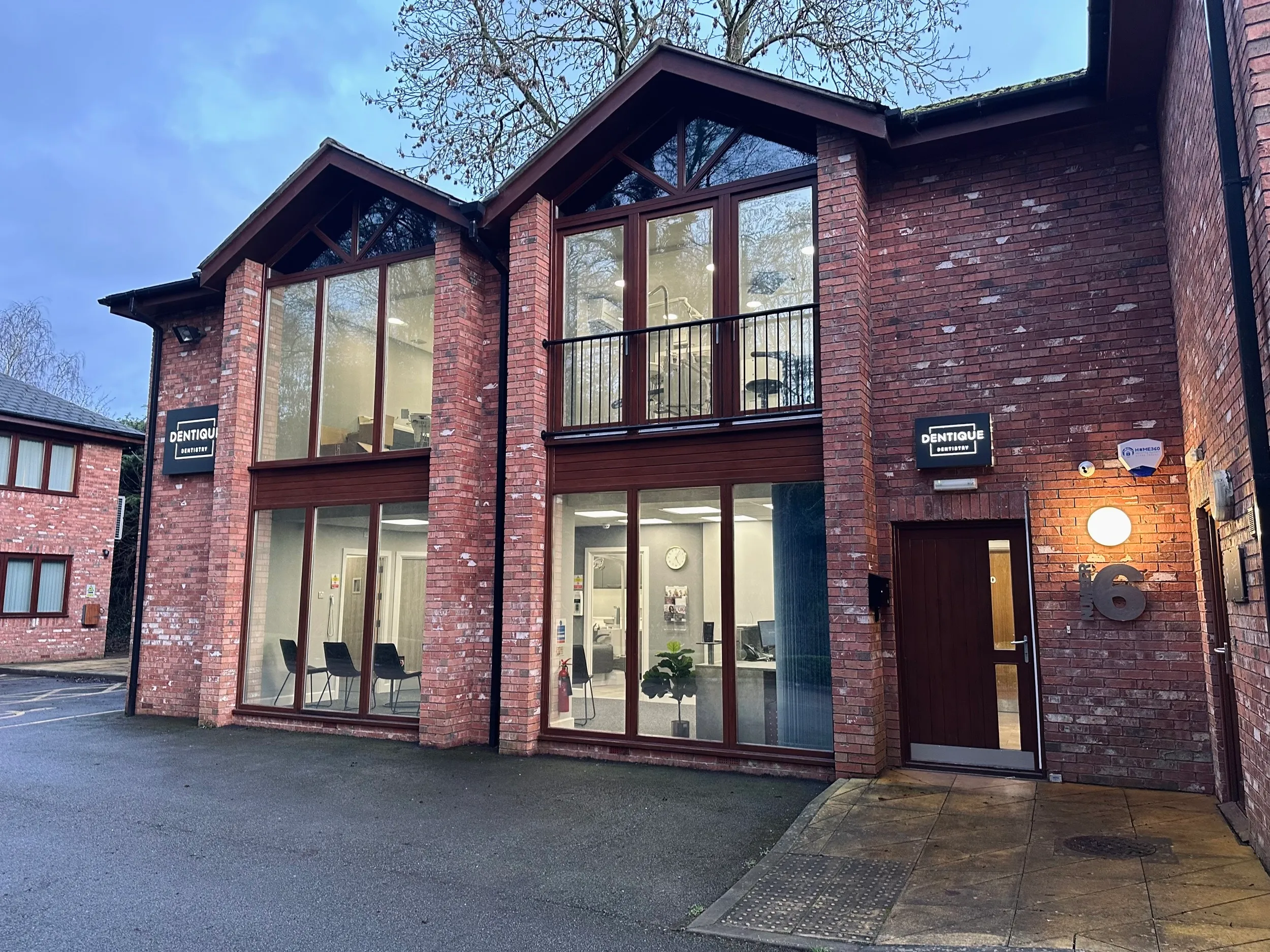 Two-story brick dental office with large windows showing a waiting room and dental chair inside, illuminated in early evening.