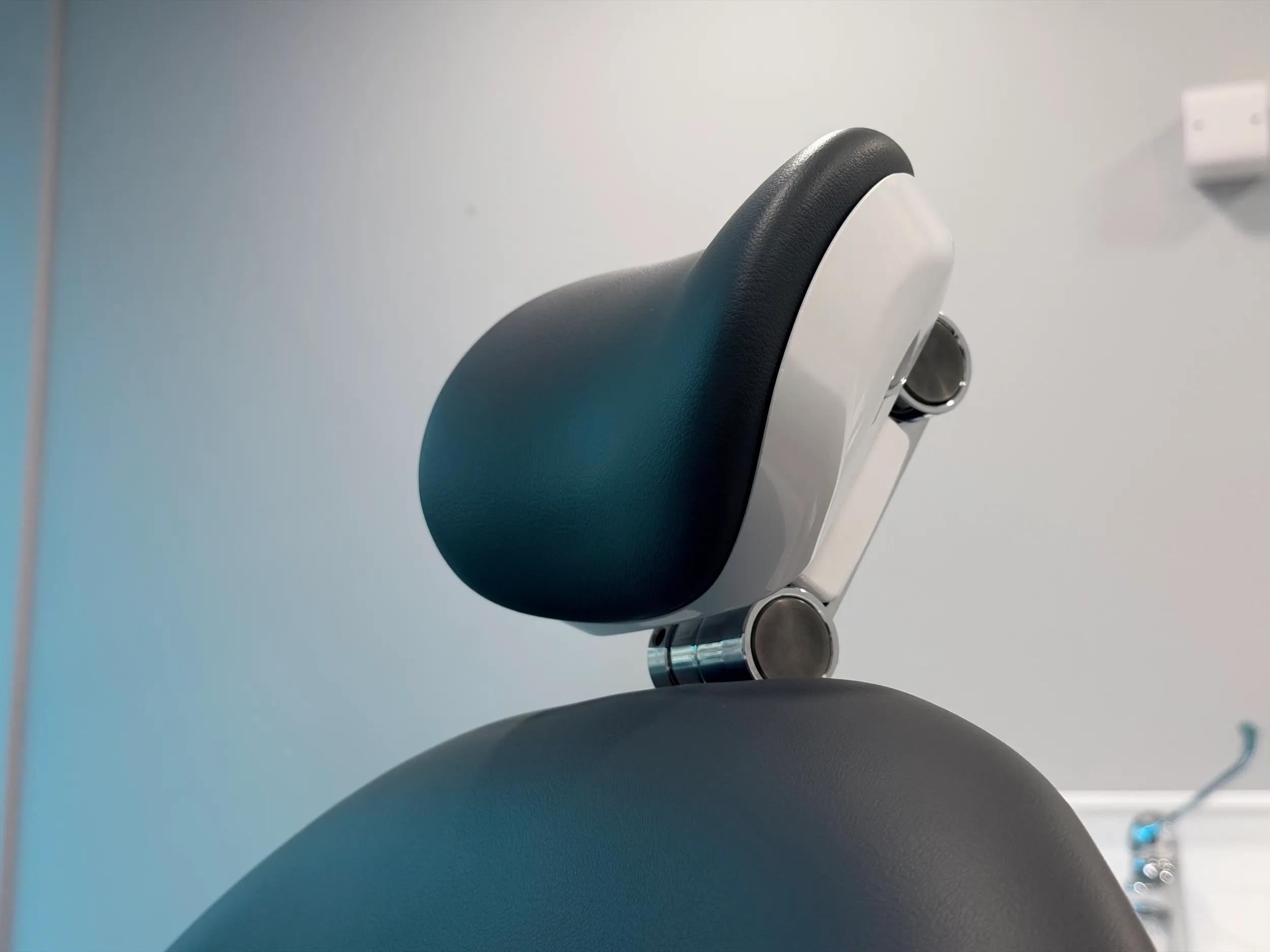 Close-up of a black and white adjustable headrest on a medical or dental chair against a plain wall.