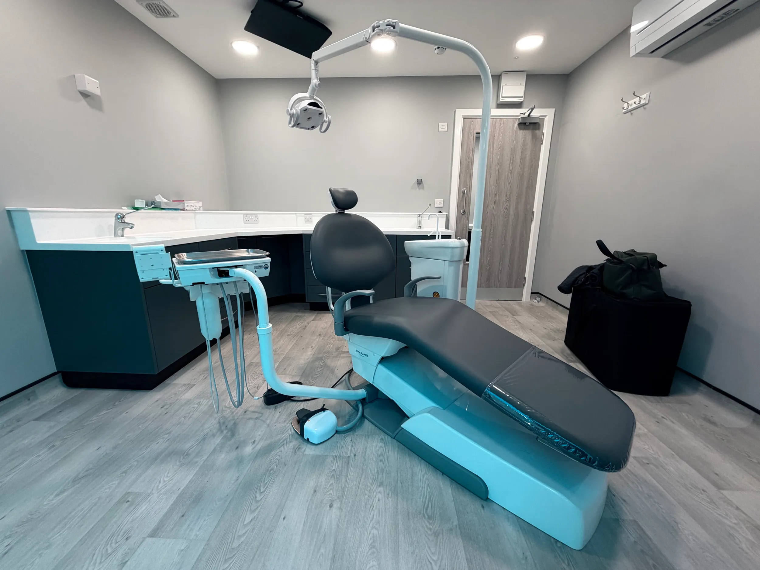 Modern dental clinic room with a black dental chair, overhead light, and cabinetry along the wall.