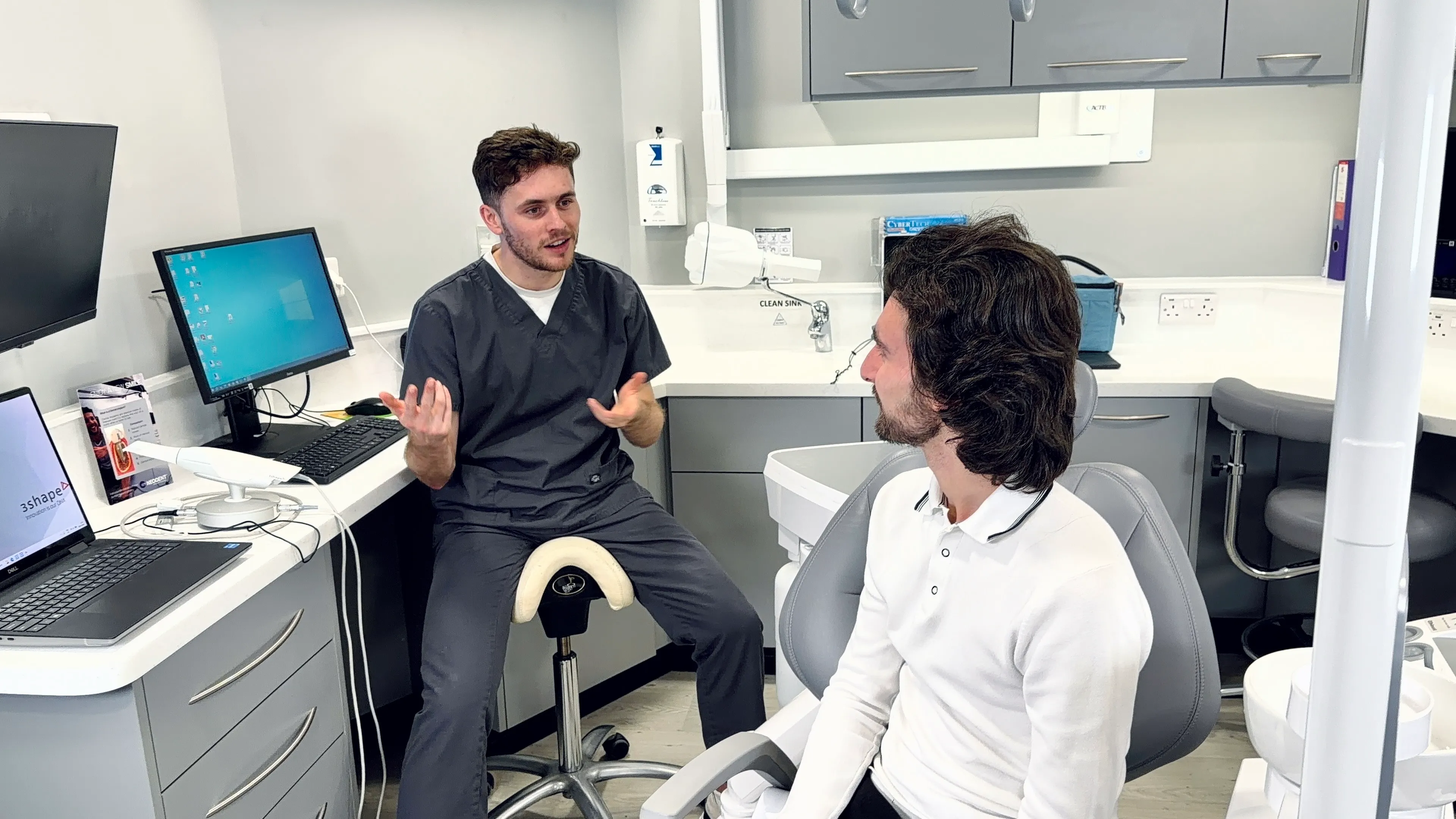 Dentist explaining treatment to patient seated in dental chair in modern clinic.
