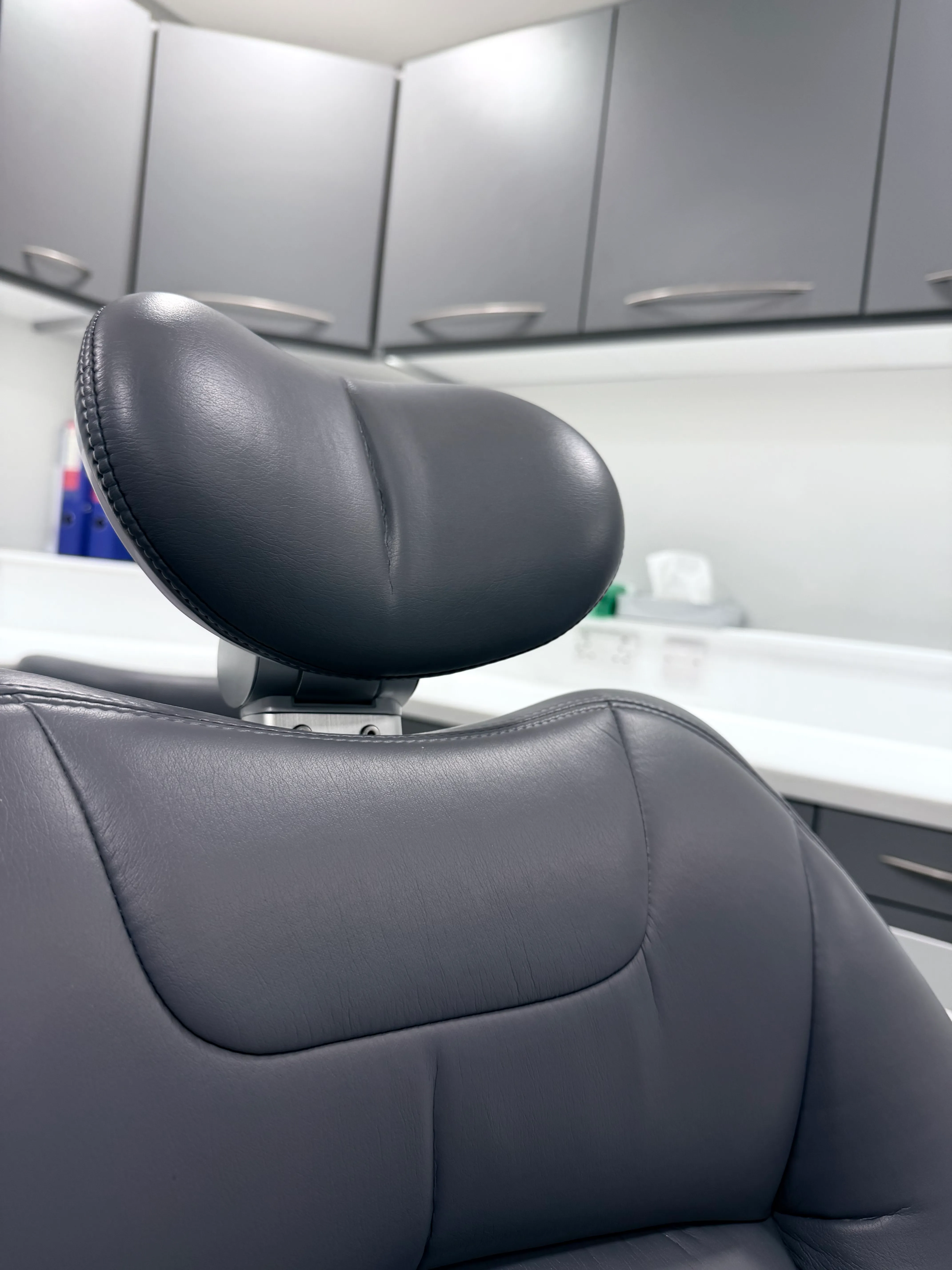 Close-up of black leather headrest and backrest of a dental chair with white cabinets in the background.