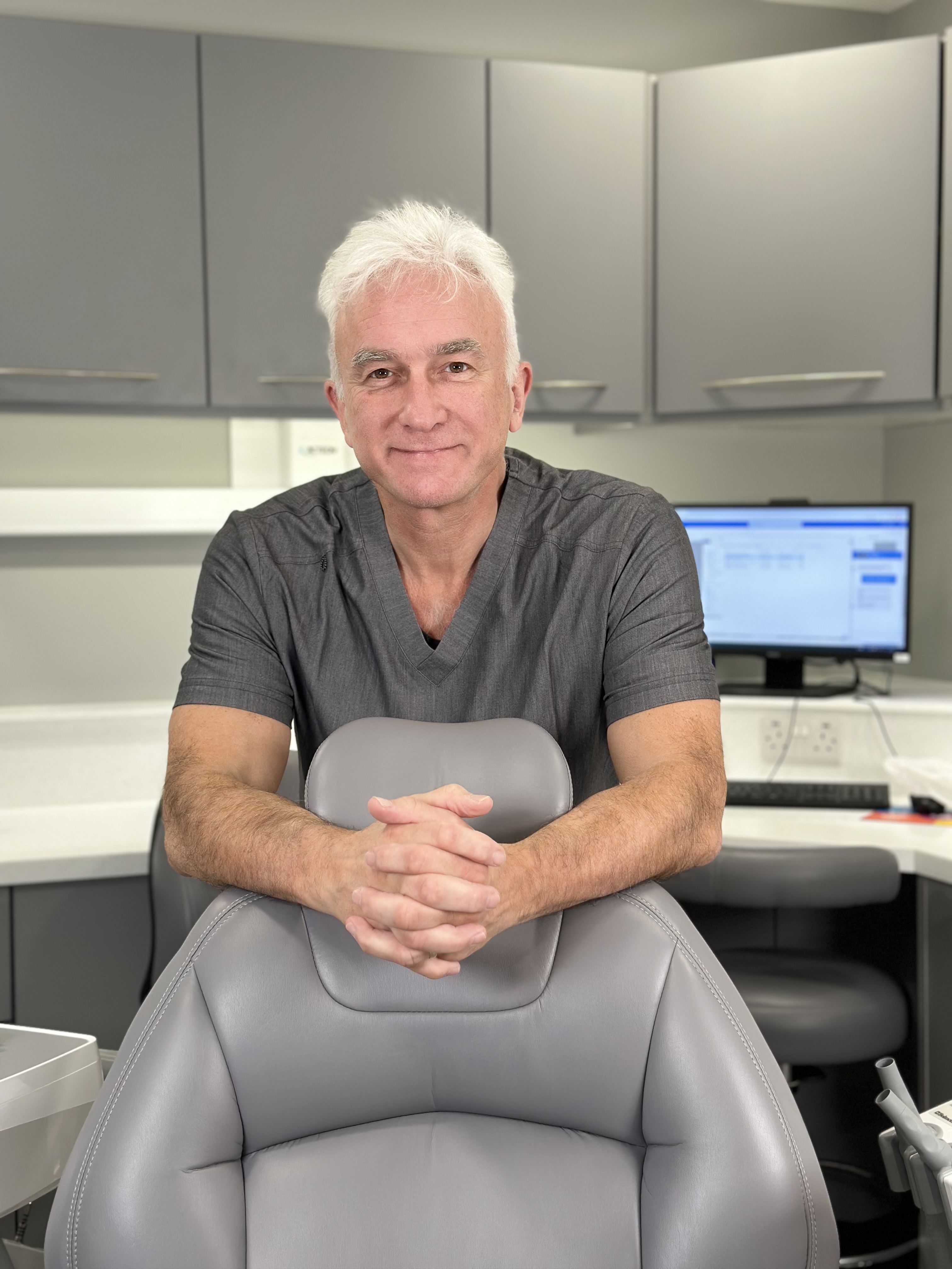 Paul Worskett leaning on the back of a grey dental chair in a dental surgery.