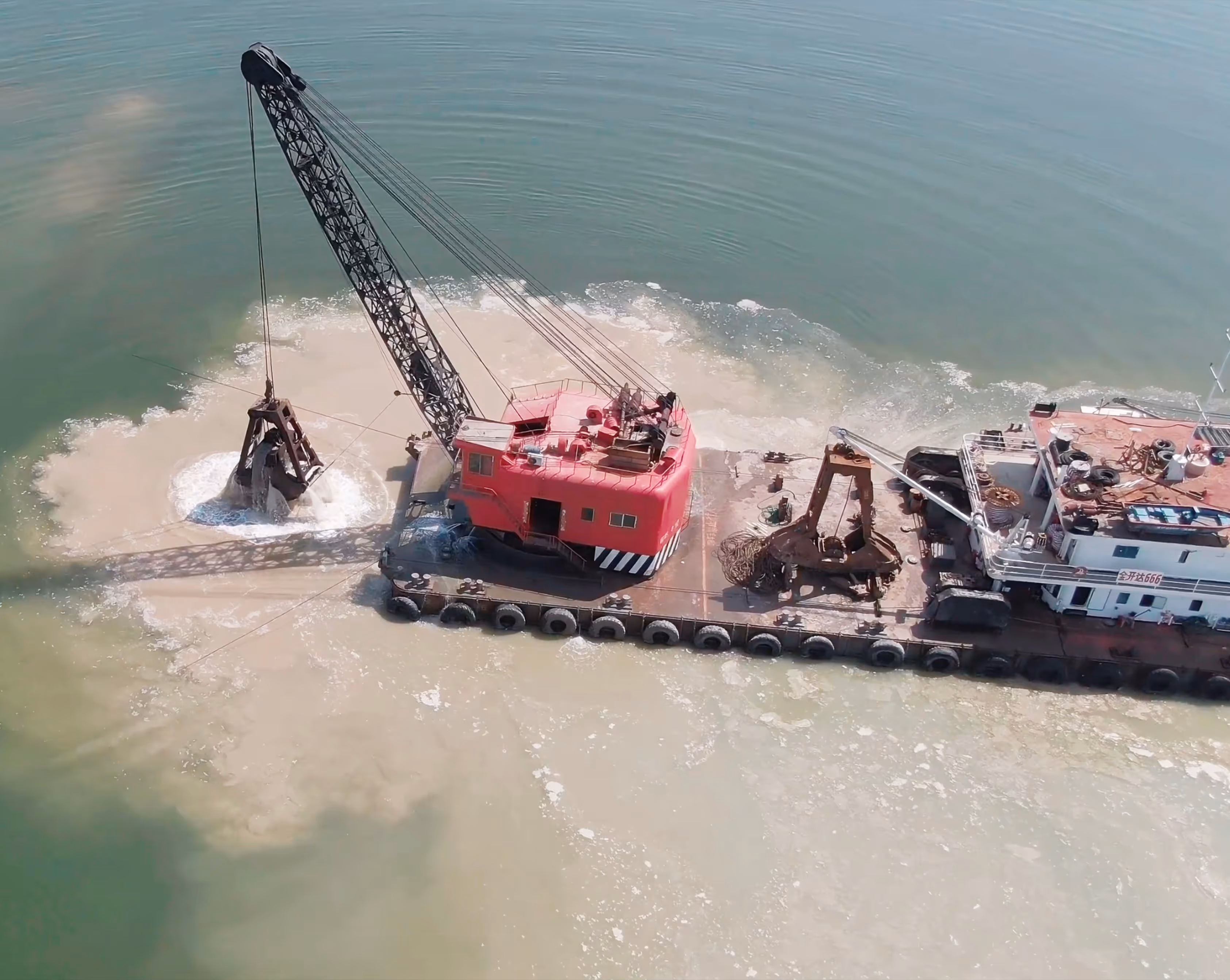 A dredging barge with a crane releasing sediment into the water, creating a large cloud of disturbed sediment.