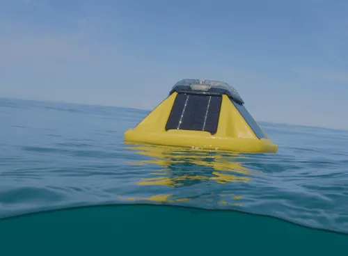Yellow buoy with solar panels floating on calm ocean water under a clear sky.