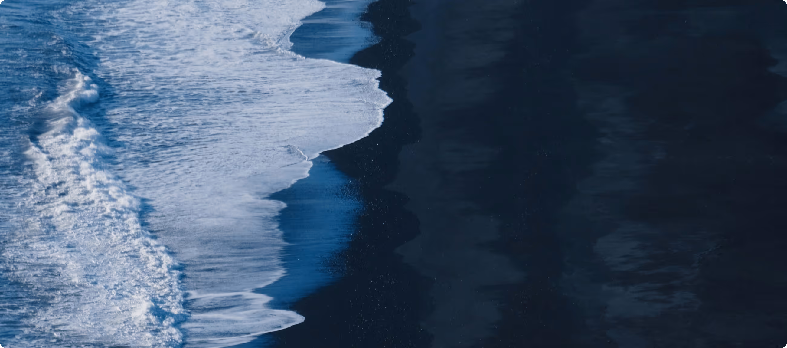 White ocean waves gently washing onto a dark sandy beach.