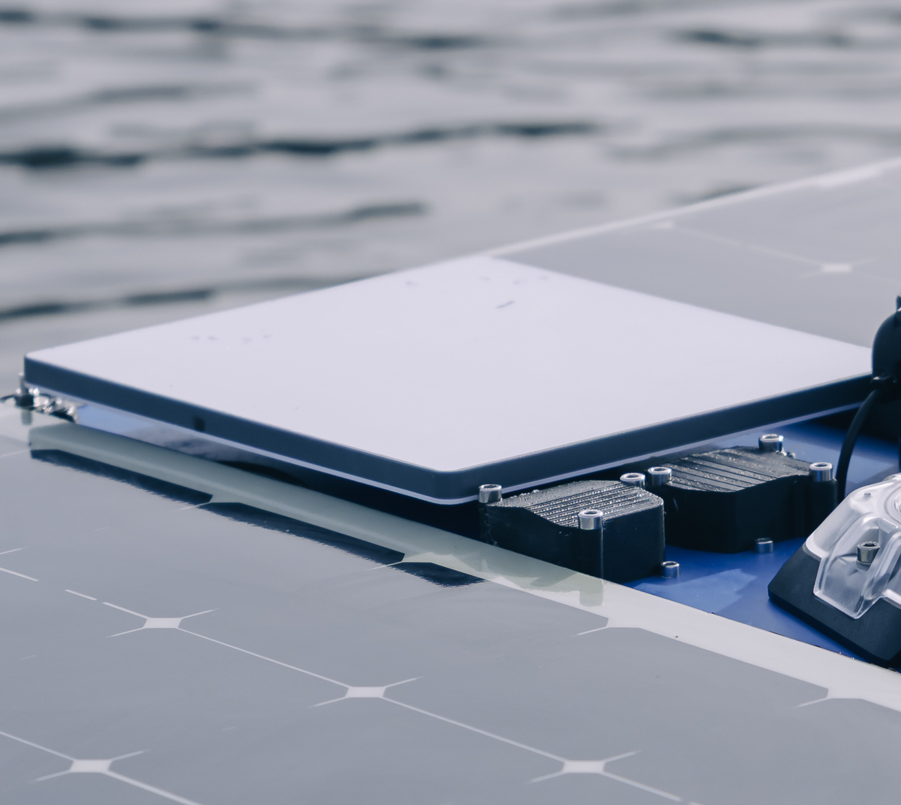 Close-up of solar panels and electronic components mounted on a surface near water.