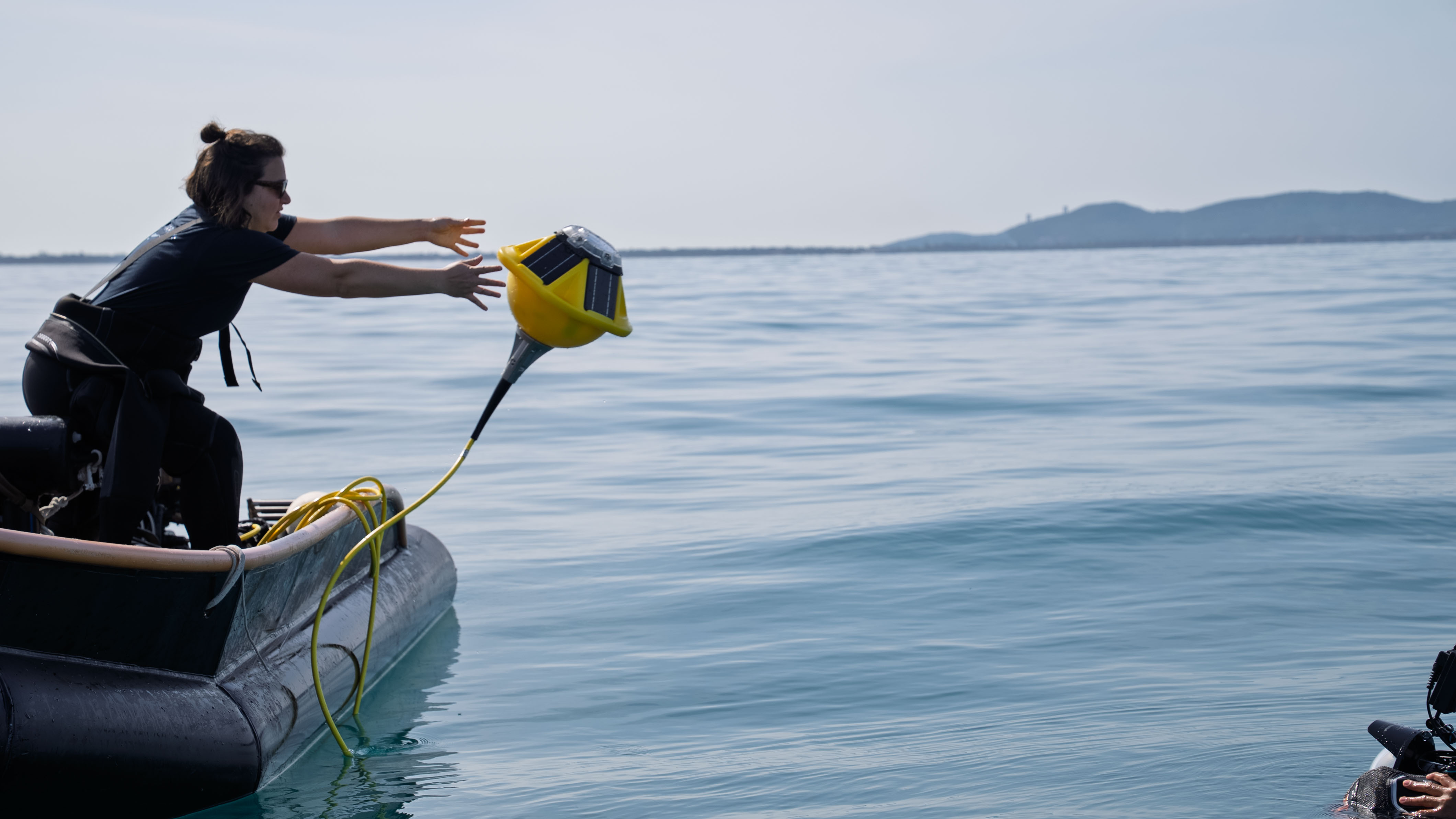Sofar Ocean team member deploying yellow Spotter buoy from inflatable boat on calm coastal waters