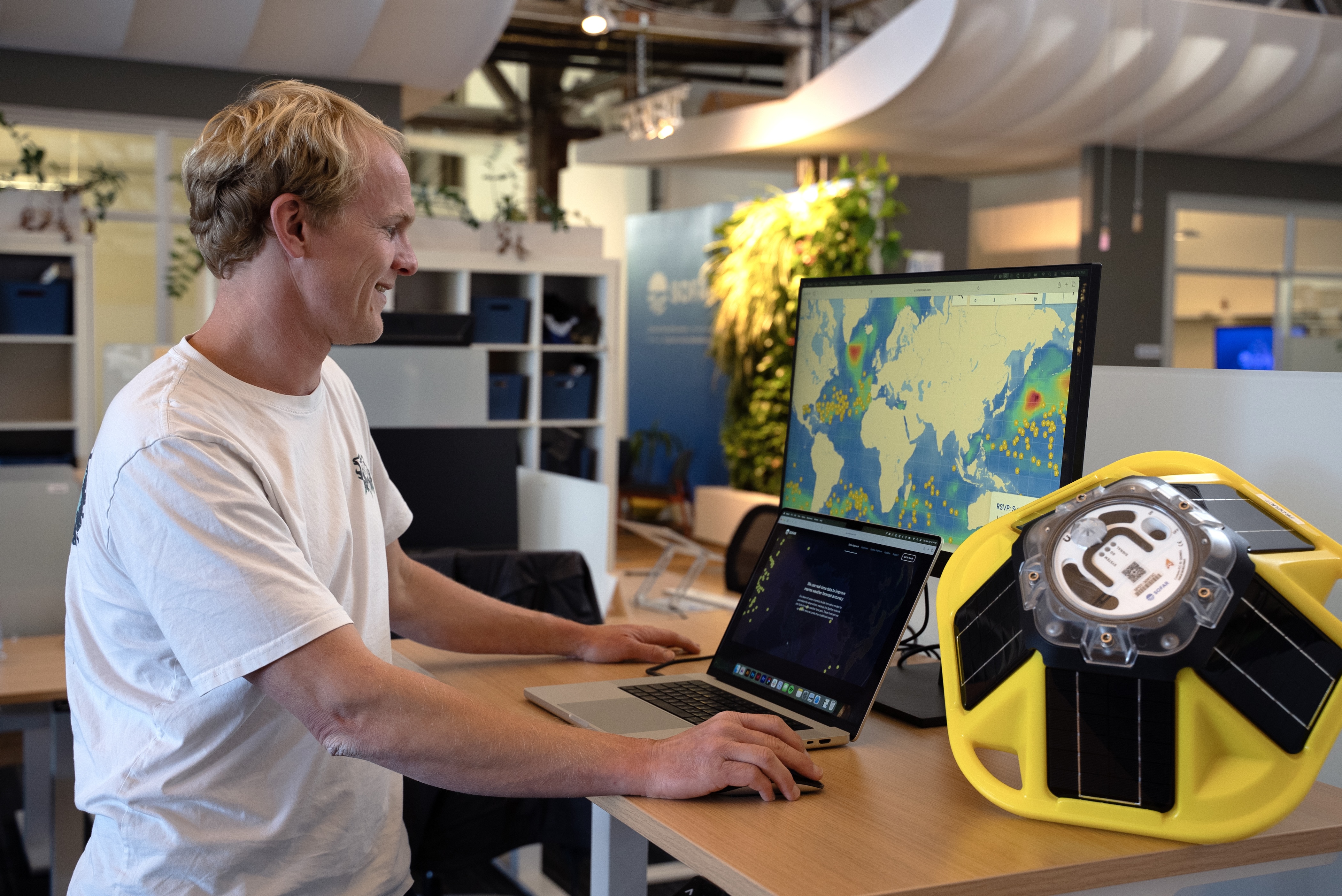Port operations staff analyzing Spotter ocean data on computer screen with yellow Spotter buoy on desk