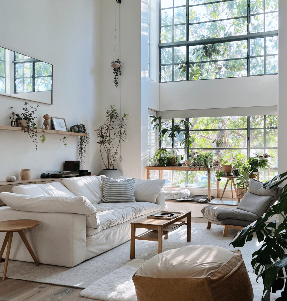A double-height living room with white sofas, plants and tall factory windows
