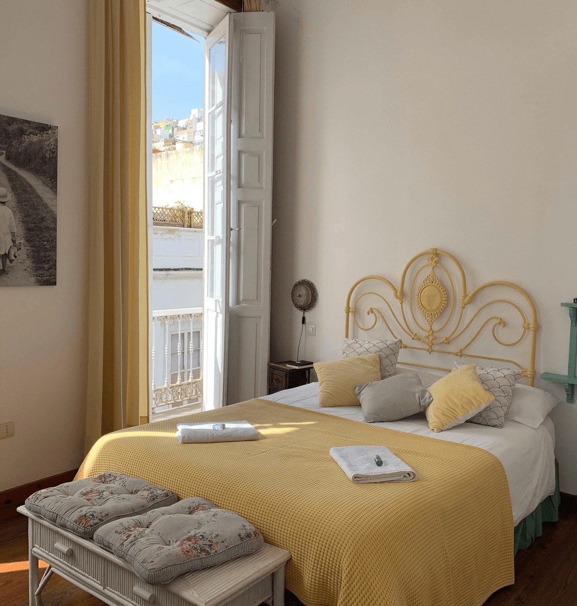 A sunlit guest bedroom with a yellow bedspread and open balcony doors