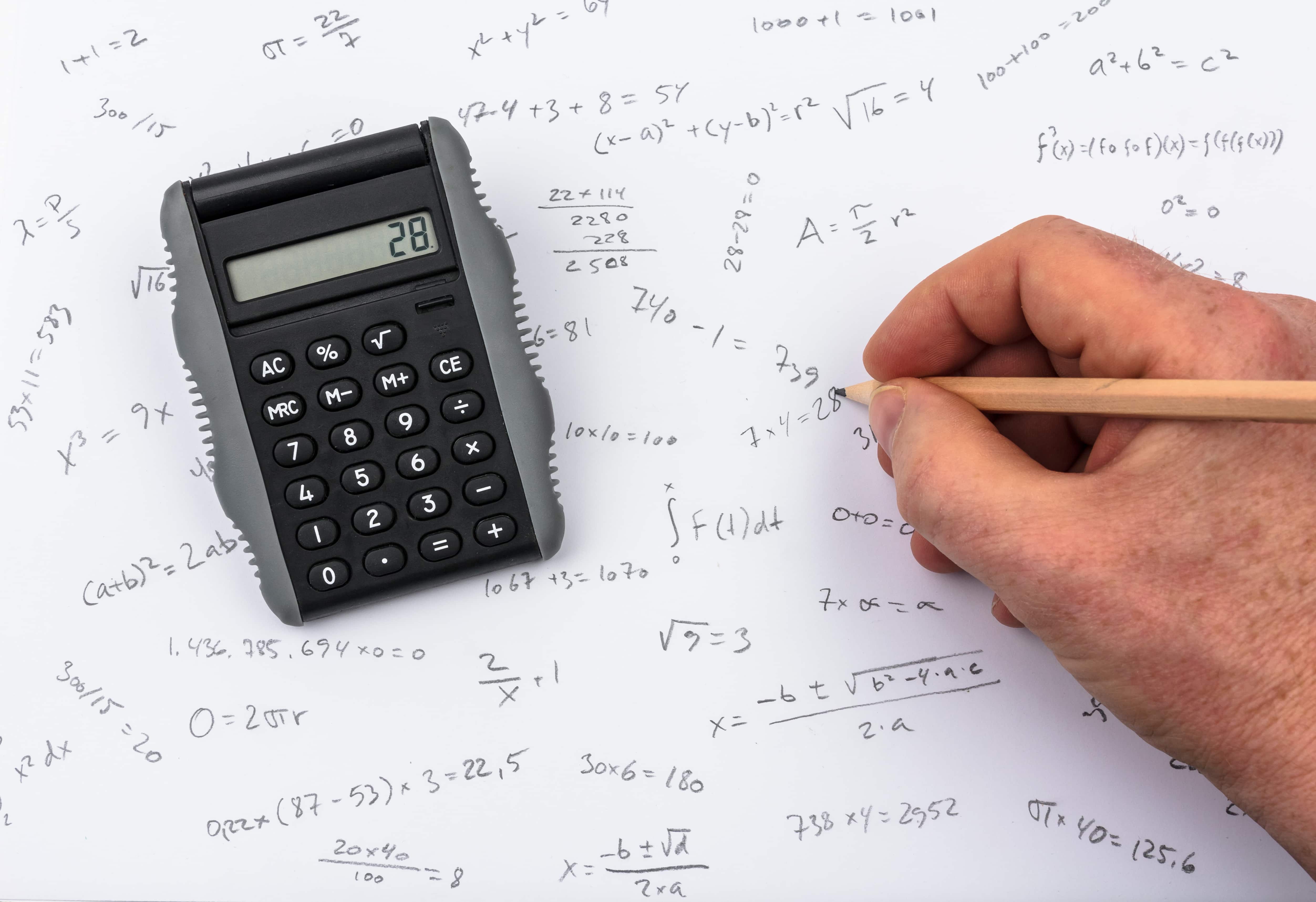 Main qui tient un stylo et écrit des formules mathématiques avec une calculatrice à coté