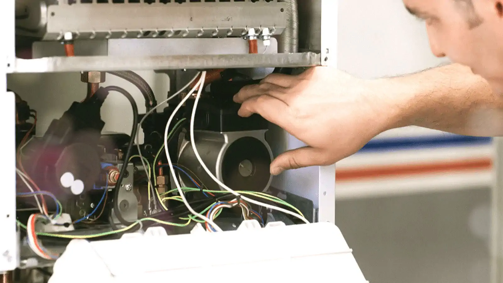 Technician installing or repairing the internal components of a furnace with various wires and mechanical parts visible.