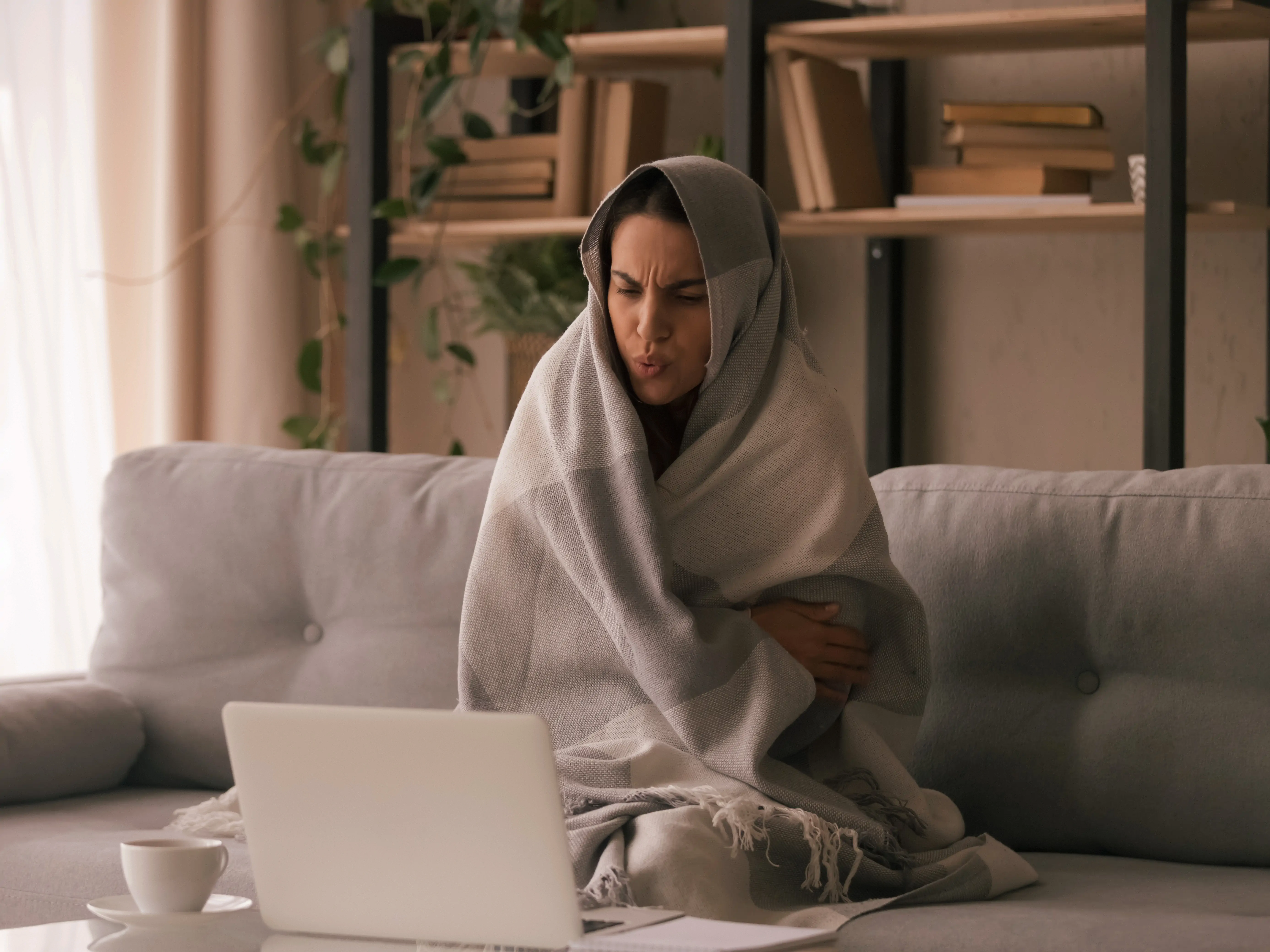 A homeowner sits on her couch with a blanket wrapped around her
