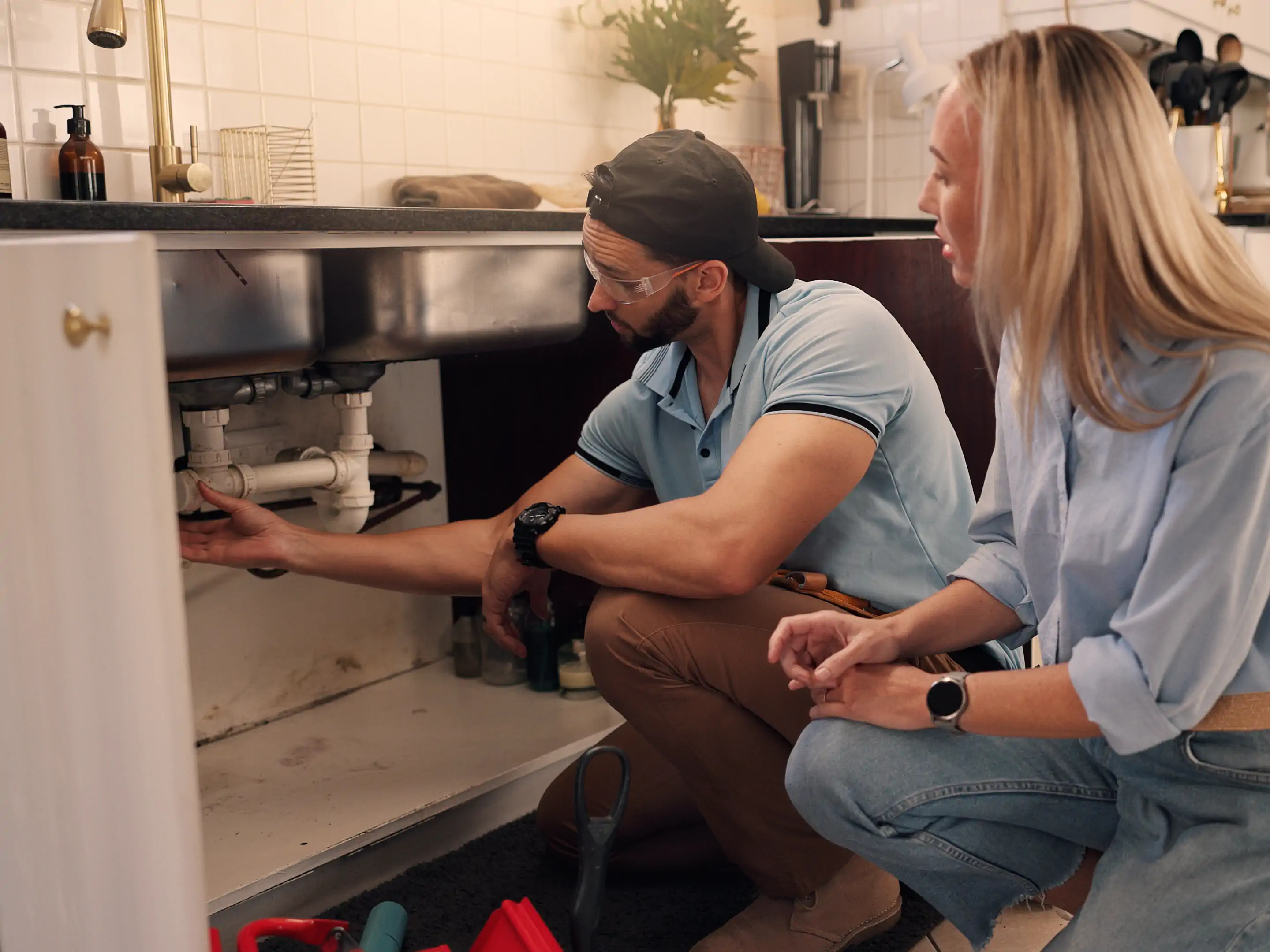 A plumber helps a homeowner with a plumbing issue under the sink