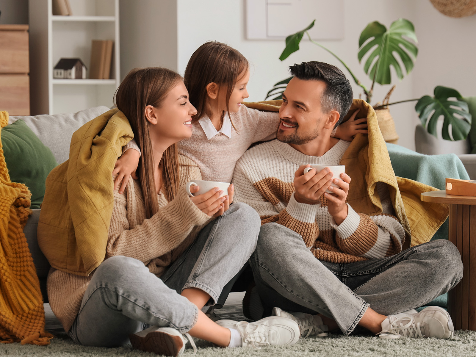 A family of 3 smiling and holding cups in their hands.