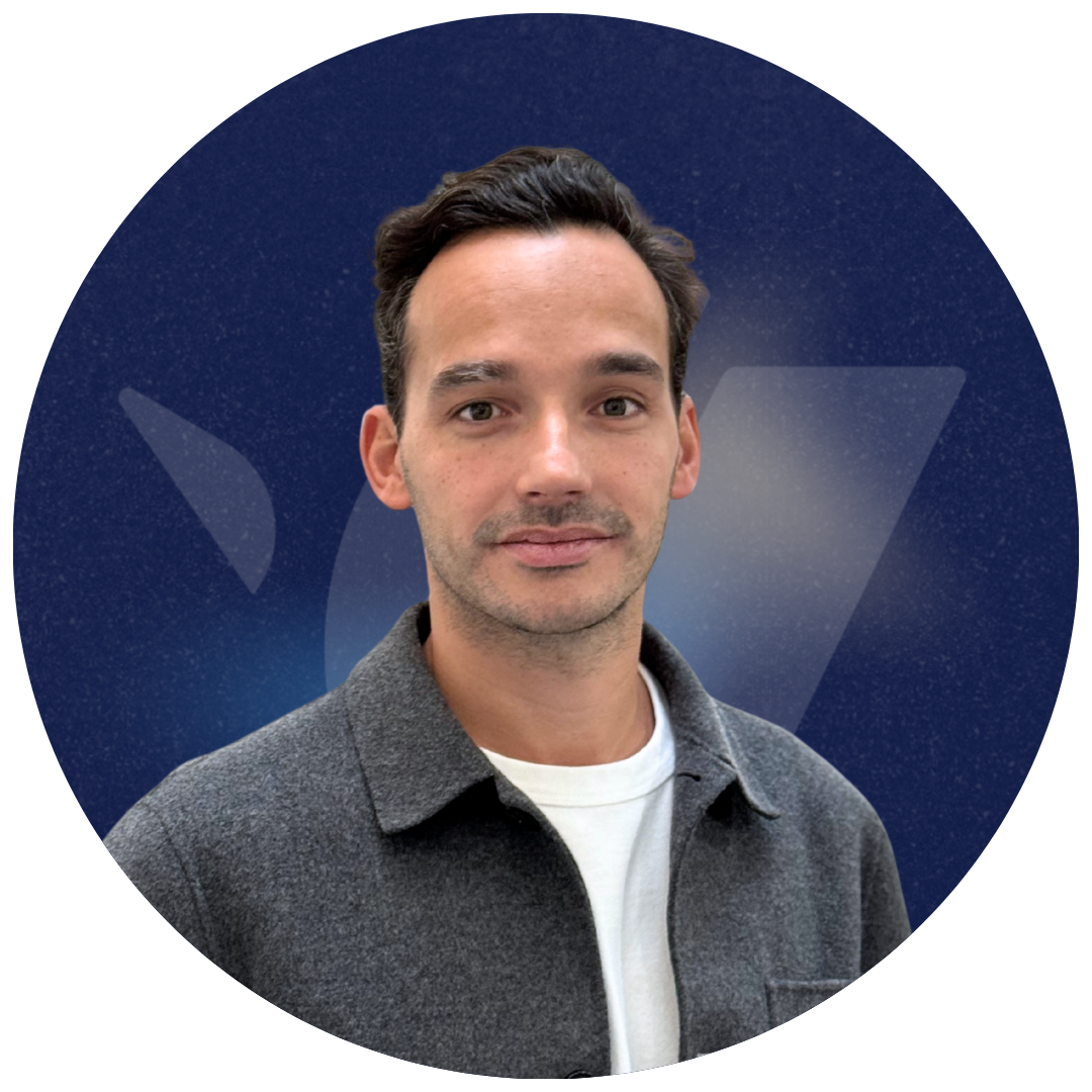 Portrait of a man with short dark hair wearing a grey coat over a white shirt against a dark blue background.