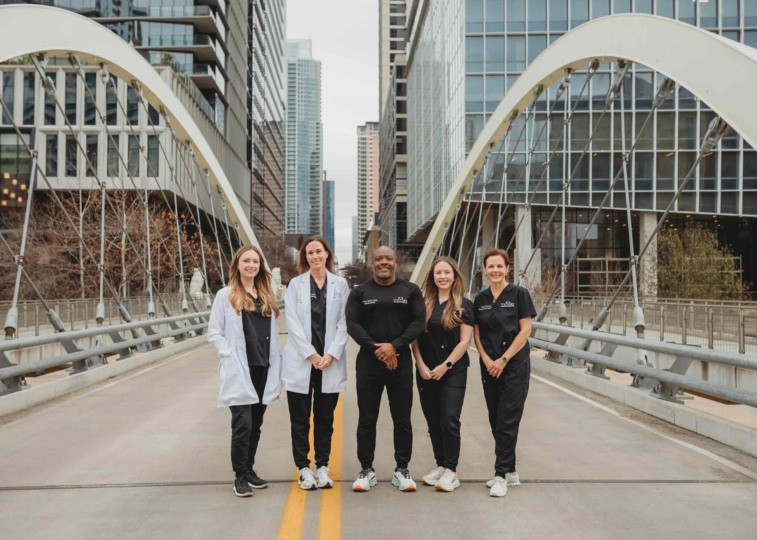 Five medical professionals standing on a city bridge with modern buildings in the background.