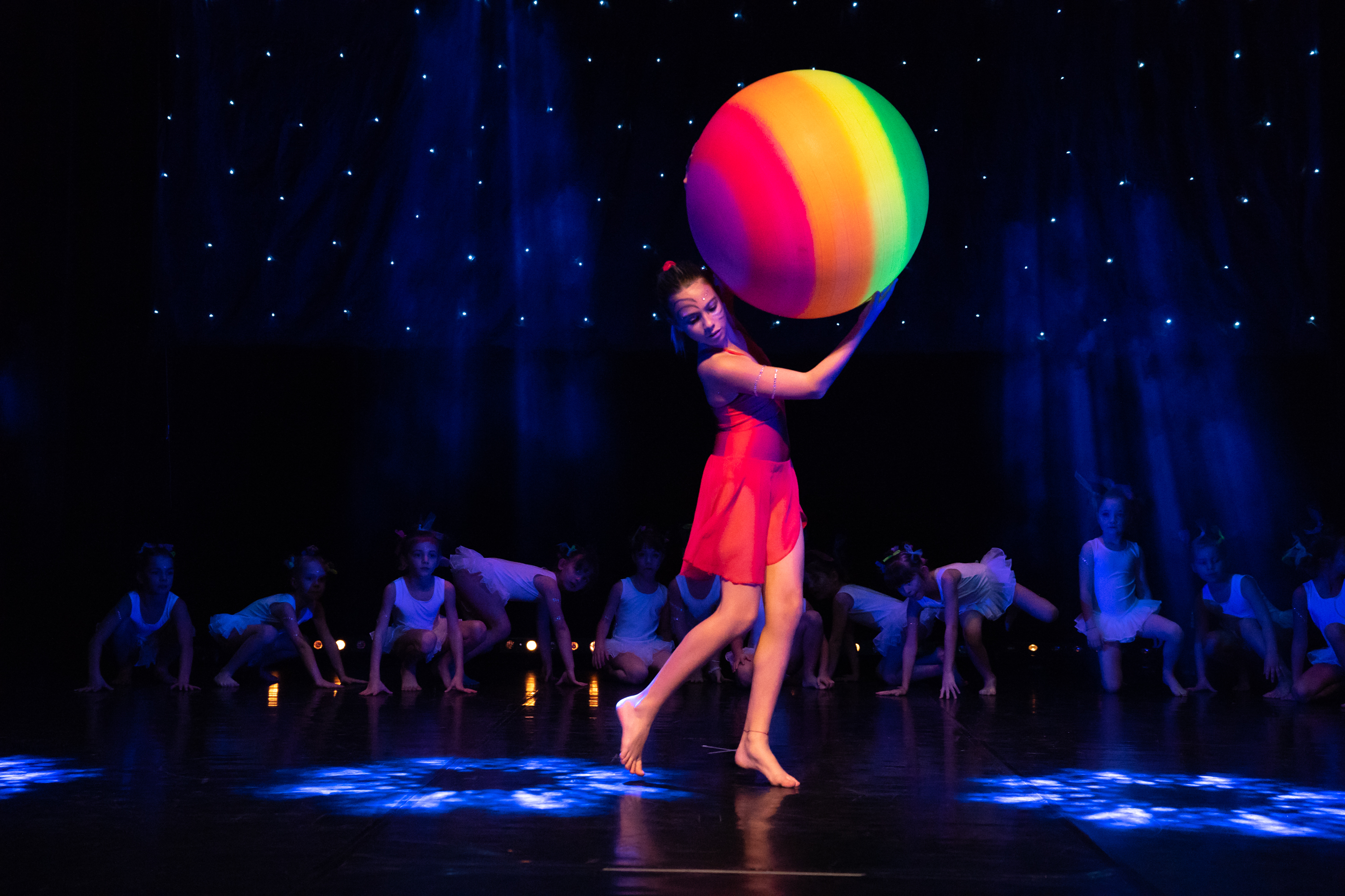 Allieva di Gym-Art-Dance solleva una palla multicolore sul palco durante lo spettacolo Arte del Movimento e del Respiro