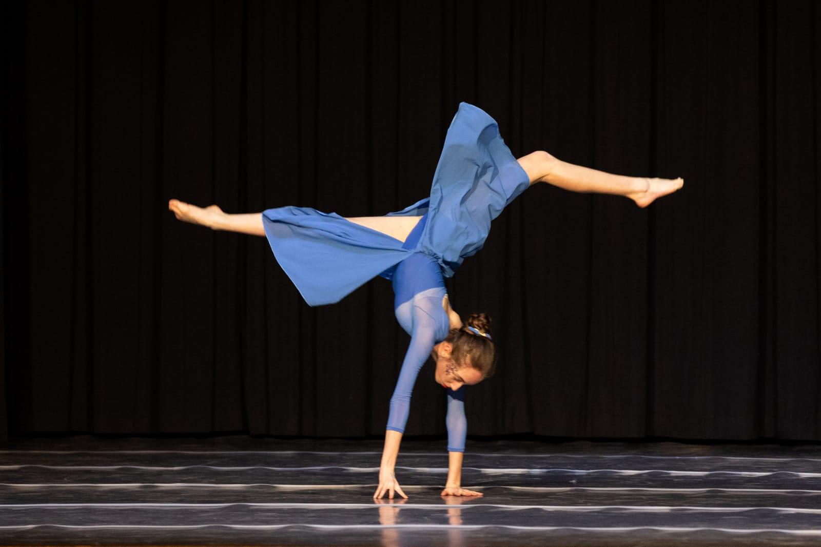Allieva in abito blu esegue una spaccata acrobatica in equilibrio sulle mani sul palco