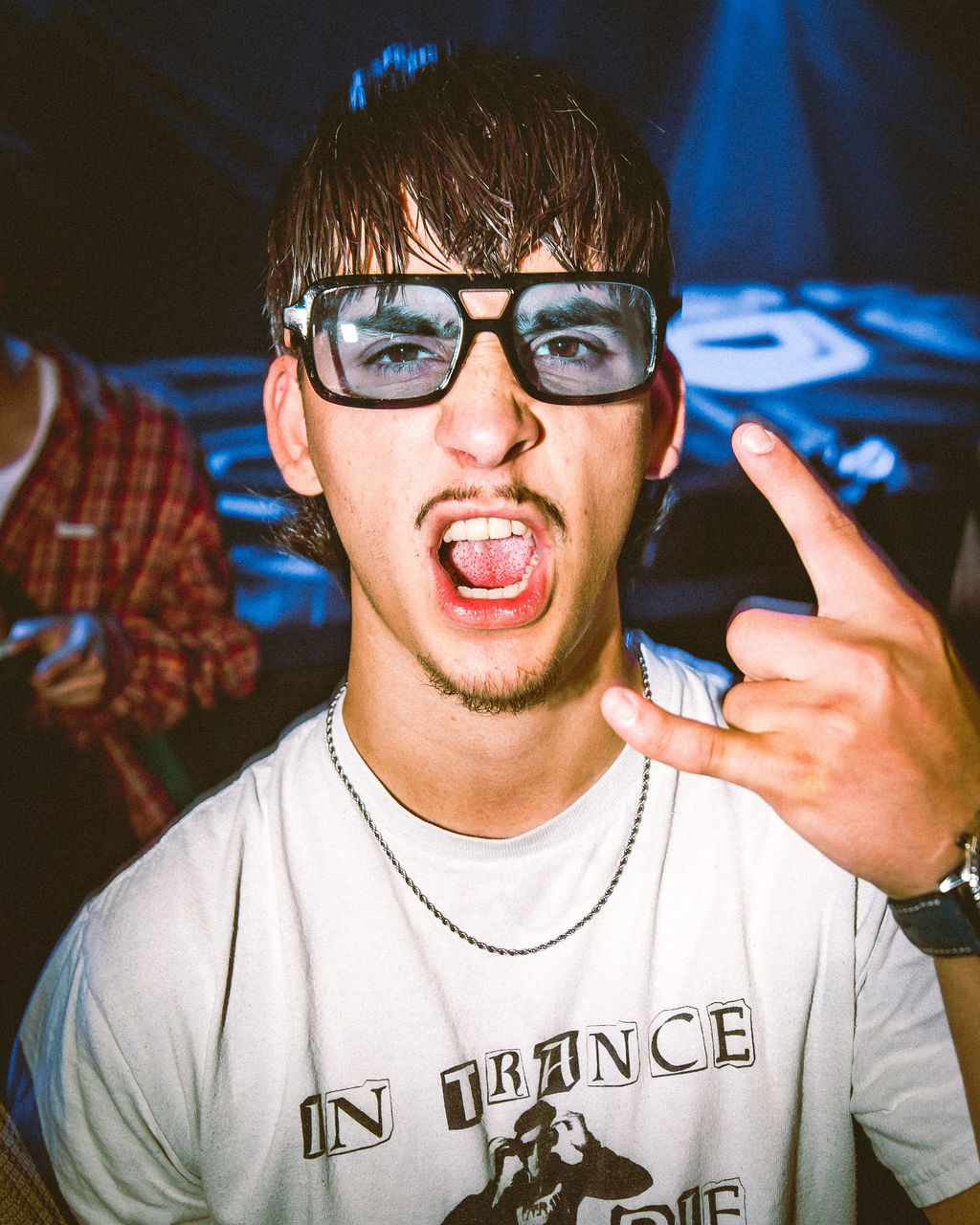 Young man with wet hair and large glasses making a rock hand gesture and shouting at a party.