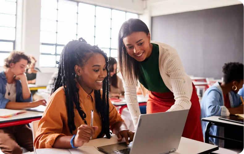 An image of a women helping a student on a laptopdent