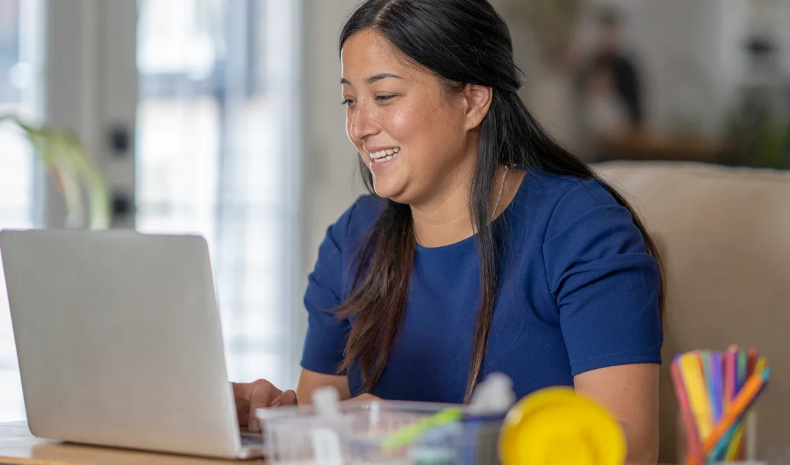 An image of a women smiling whilst looking at here computer 