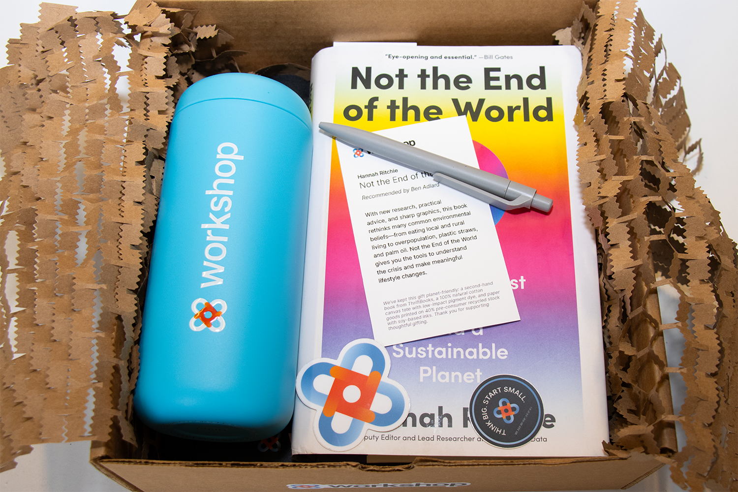 Cardboard box with Workshop branded water bottle, a book titled 'Not the end of the world', and Workshop branded pen
