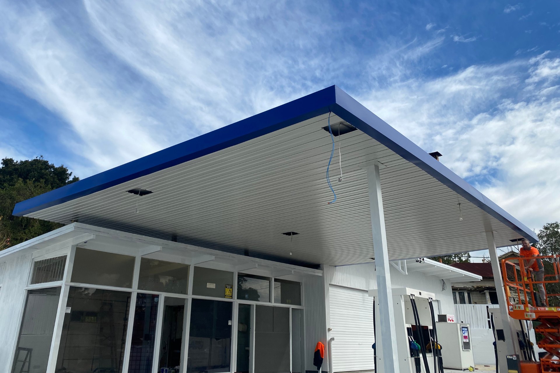 A petrol station undergoing upgrades with a newly installed flat metal roofing canopy in blue over existing fuel pumps.