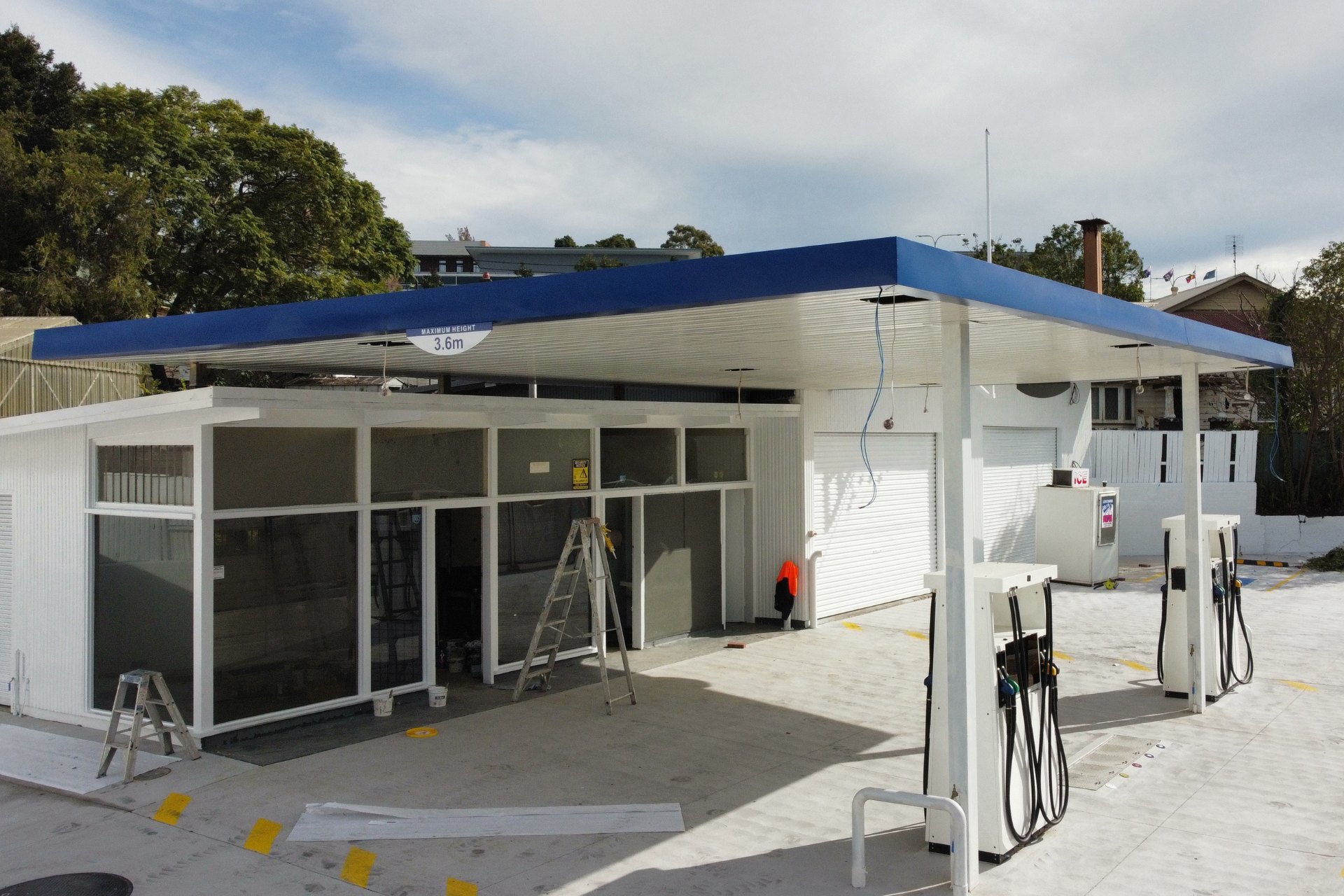 A petrol station undergoing upgrades with a newly installed flat metal roofing canopy in blue over existing fuel pumps.