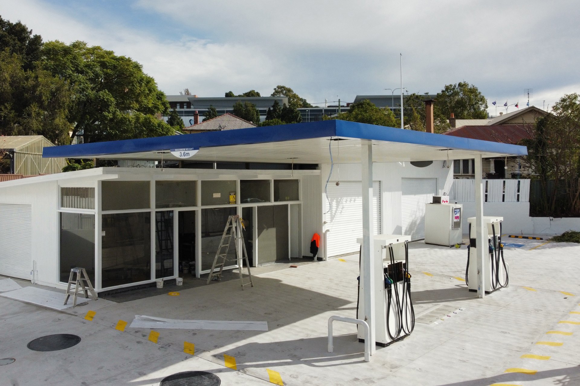 A petrol station undergoing upgrades with a newly installed flat metal roofing canopy in blue over existing fuel pumps.