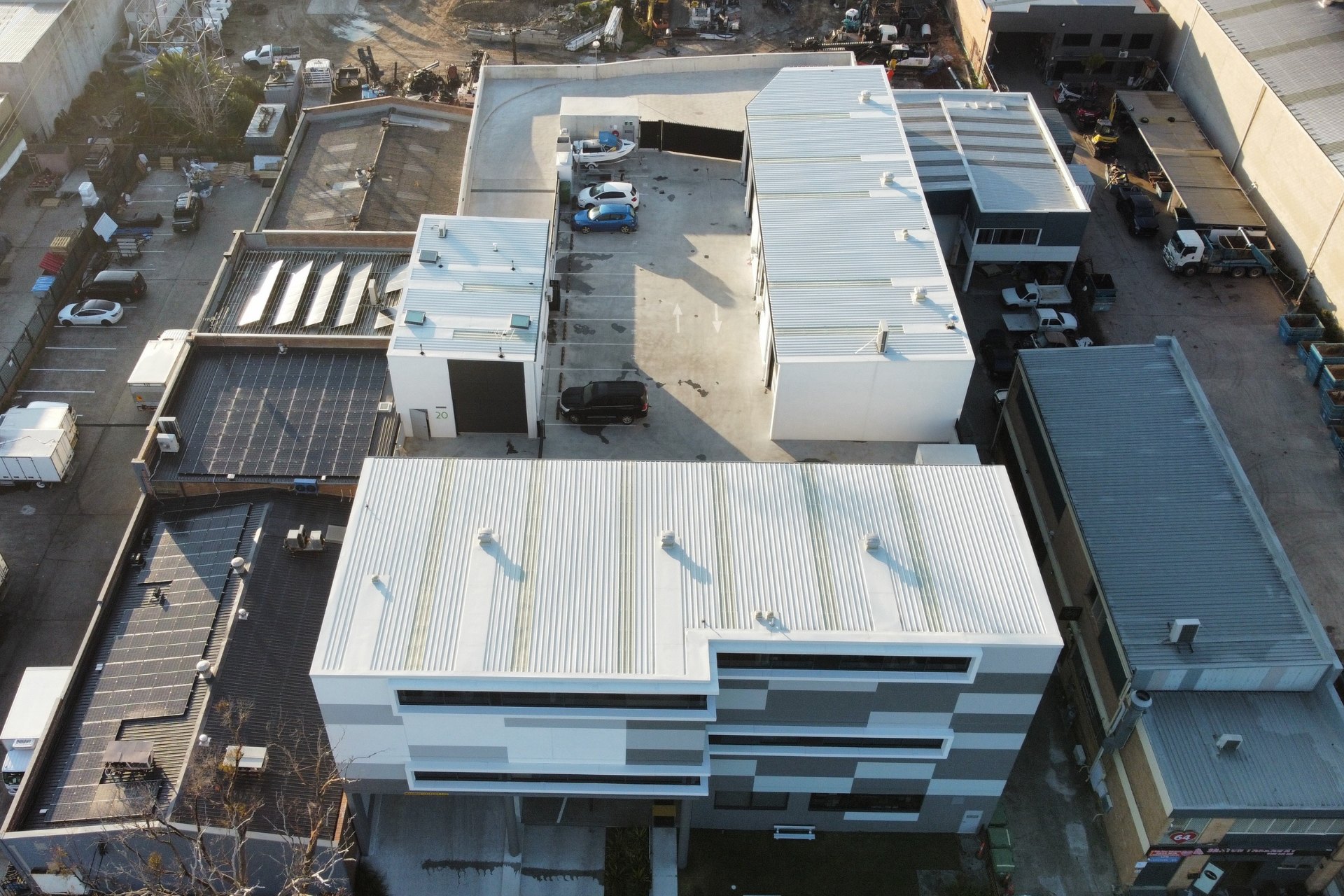 Modern commercial building with a geometric facade and clean commercial and industrial metal roofing. The structure sits in an urban setting with surrounding warehouses and roads.