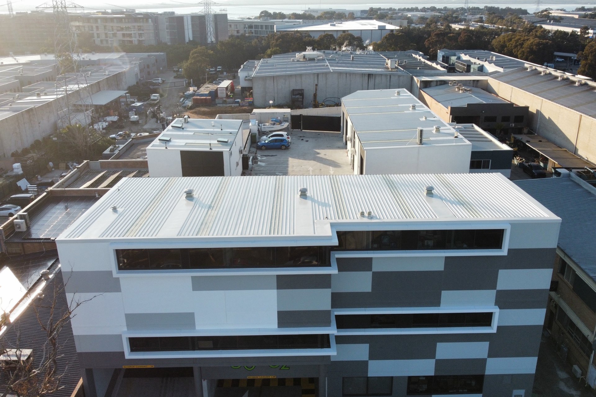 Modern commercial building with a geometric facade and clean commercial and industrial metal roofing. The structure sits in an urban setting with surrounding warehouses and roads.