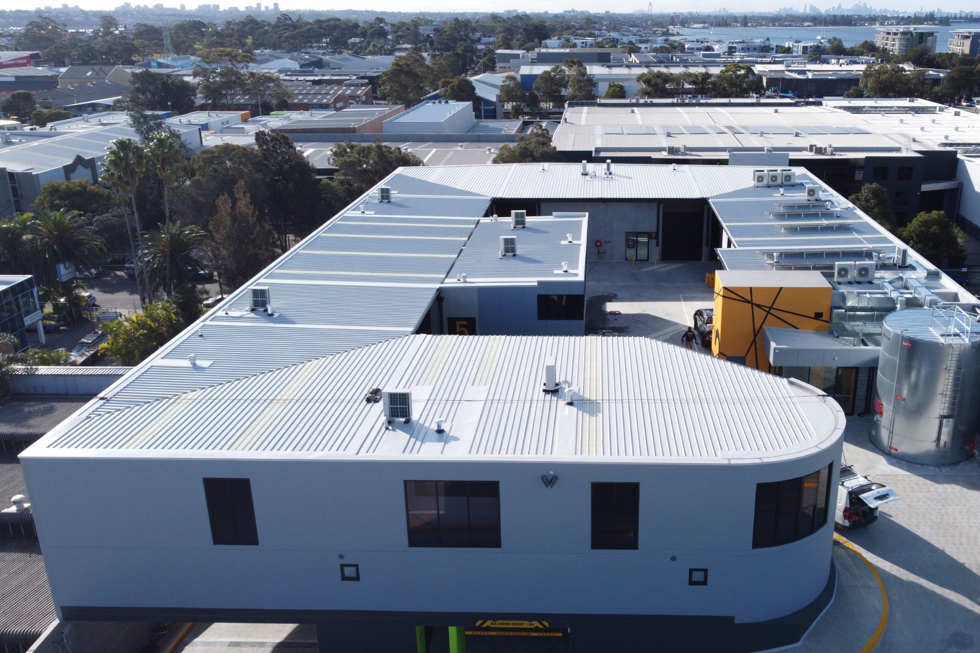 Aerial view of a commercial building complex featuring clean, new metal roofing with visible HVAC units and skylights, surrounded by an urban industrial area.