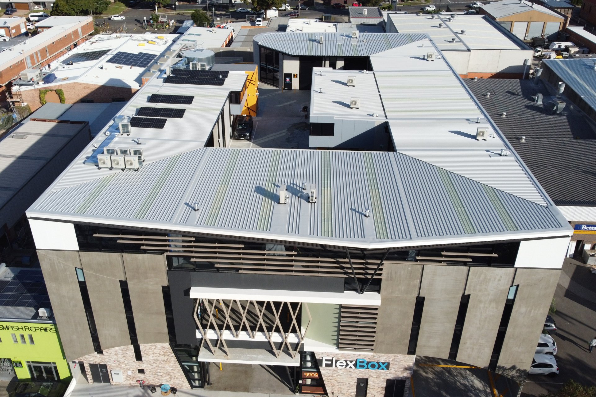 Aerial view of a commercial building complex featuring clean, new metal roofing with visible HVAC units and skylights, surrounded by an urban industrial area.