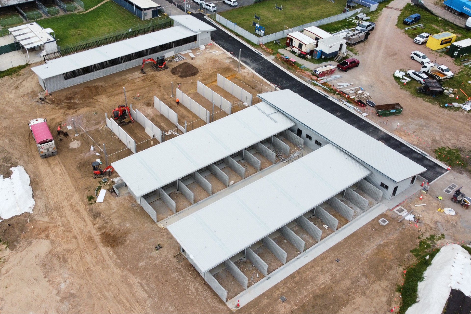 Construction site featuring a block of open stalls with clean, light-colored industrial roofing.