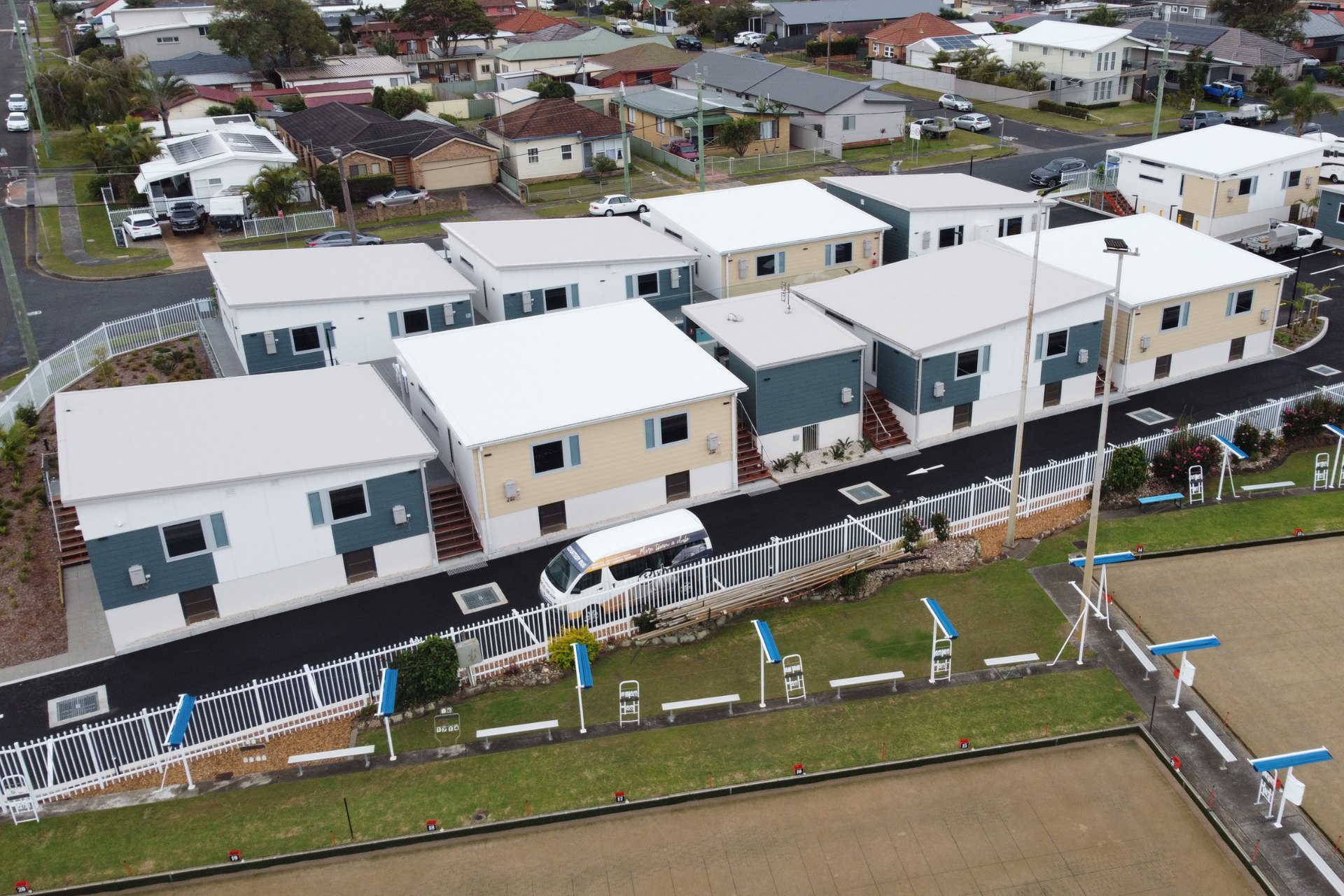 New motel development featuring rows of compact buildings with fresh white new commercial roofing. The clean, uniform roofs complement the modern exterior designs, set beside a lawn bowling green and residential neighborhood.
