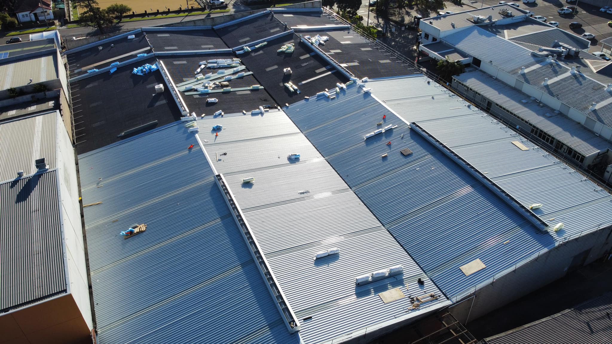 Aerial view of an industrial complex with newly installed corrugated metal roofing, showing stacked insulation materials and tools scattered across the roof surface. The clean, reflective finish highlights recent work by Element Metal Roofing.