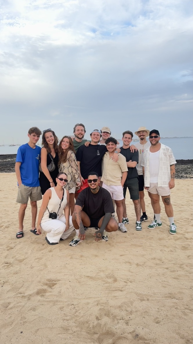 Groepsfoto van het team op het strand, samen poserend in een ontspannen en zomerse sfeer.