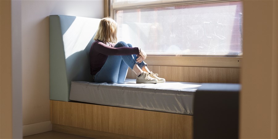 Jongere zit alleen in een vensterbank en kijkt naar buiten