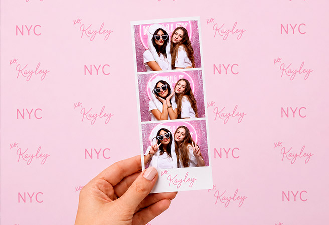 Hand holding a photo strip of two women posing with sunglasses against a pink NYC and Kayley backdrop.