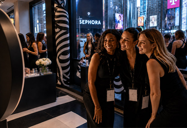 Three smiling women posing for a photo inside a Sephora store near a large window with views of New York City.