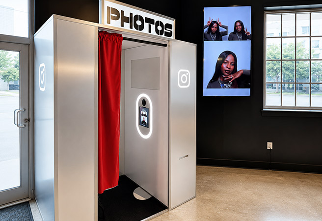 Modern photo booth with red curtain and screen displaying pictures of a woman posing.