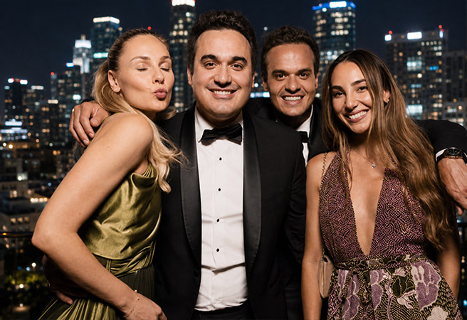 Four people dressed formally smiling and posing against a Los Angeles skyline at night.