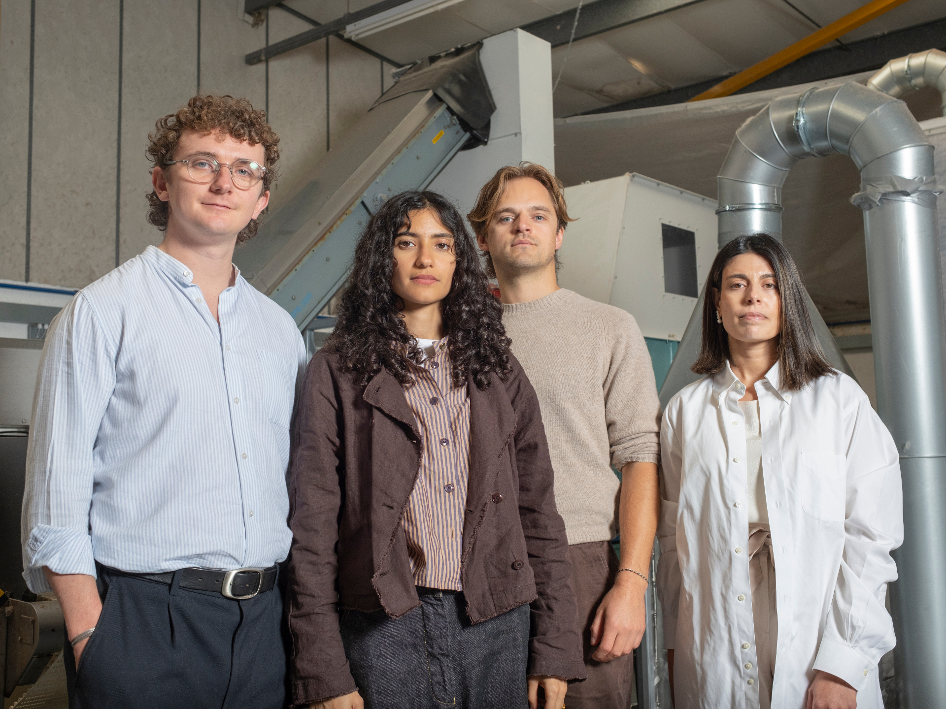 Four diverse young professionals standing indoors with industrial equipment in the background.