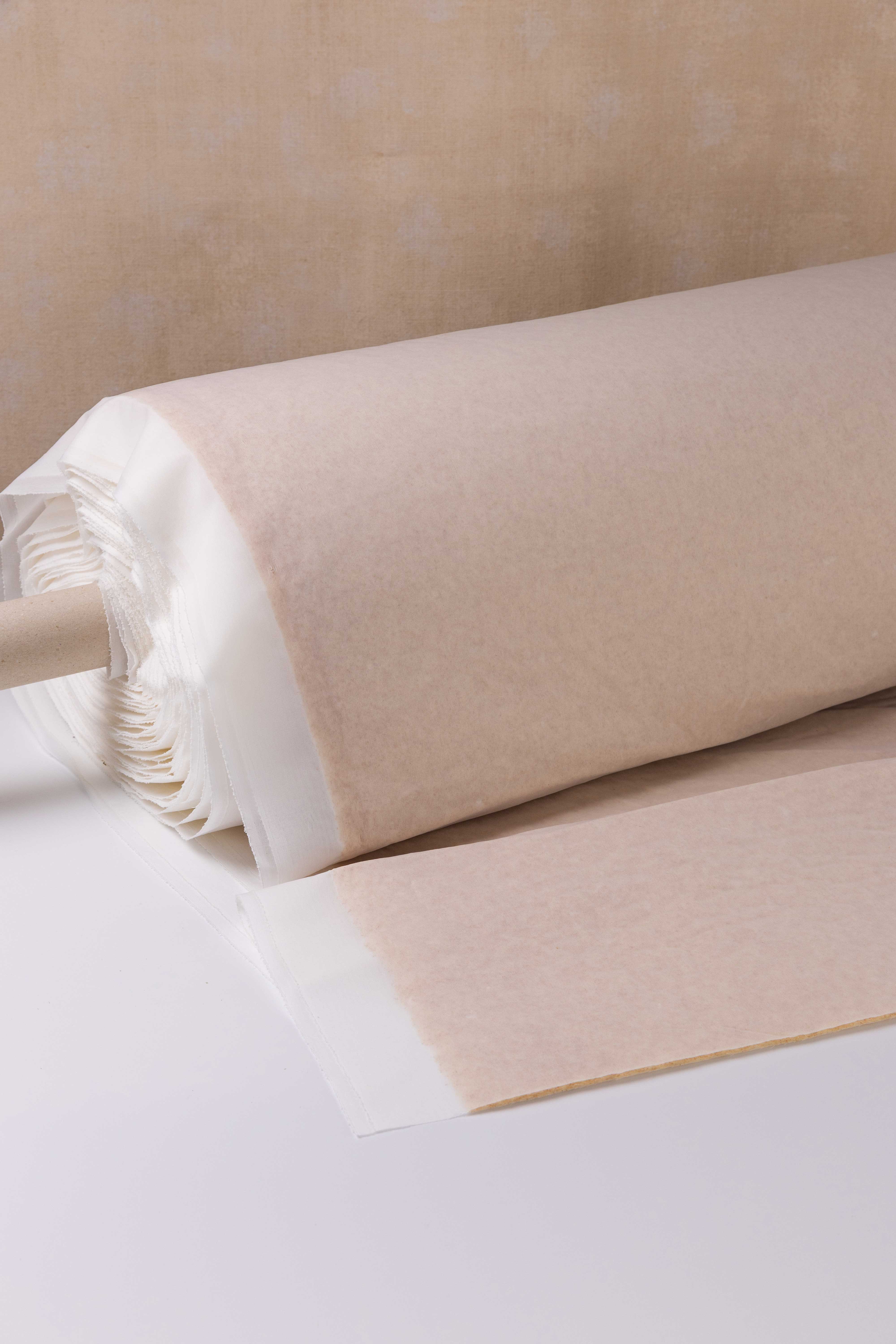 Roll of white fabric partially covered with beige interfacing material on white surface.