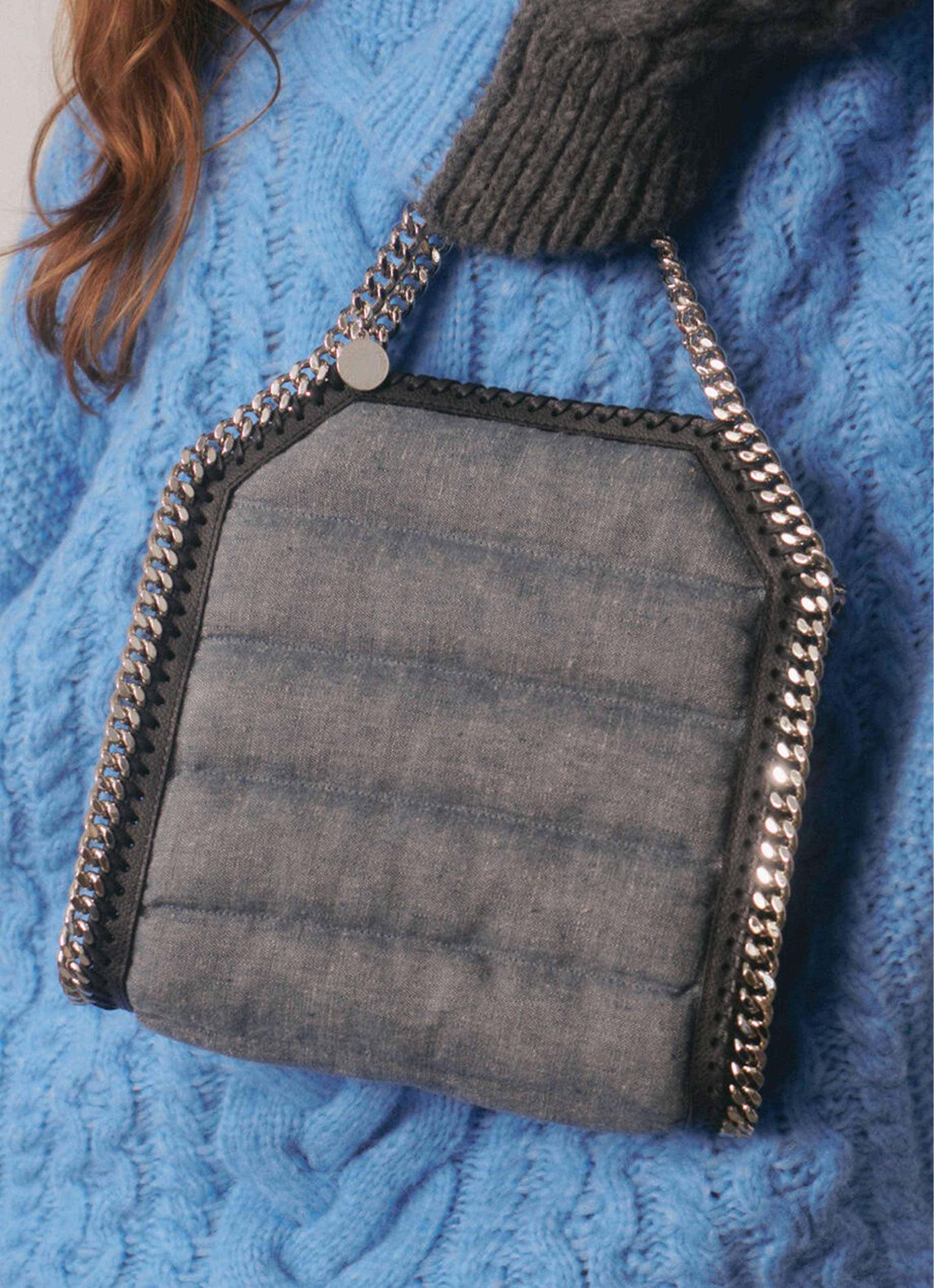 Quilted gray handbag with silver chain strap held against a blue cable-knit sweater.