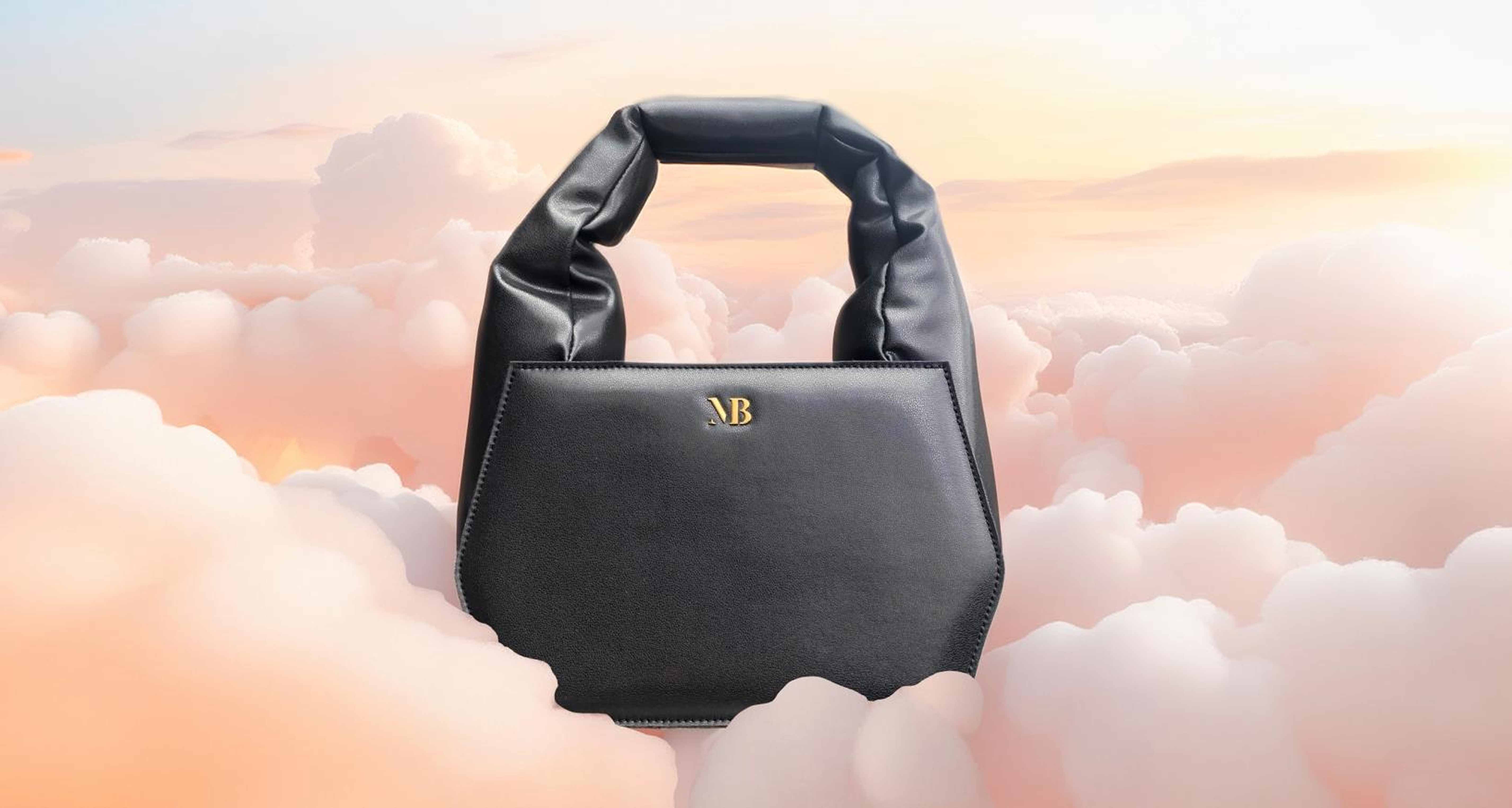Black designer handbag with padded handle and gold AB logo floating among pastel pink clouds.