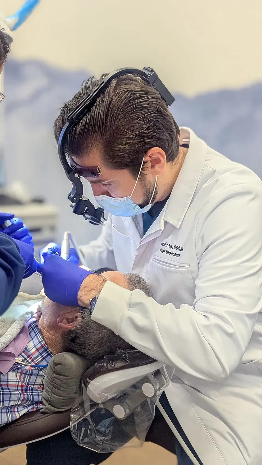 Dentist wearing magnifying loupes and gloves performing dental treatment on a patient reclining in a dental chair.