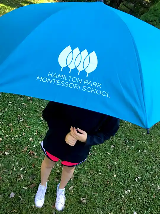 Custom 56-inch teal golf umbrella with white printed Montessori school logo in PMS matched colors